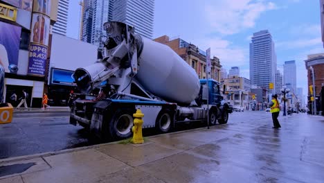 Camiones-De-Cemento-Dirigidos-Por-Un-Controlador-De-Tráfico-Sobre-Young-Y-Charles-En-El-Centro-De-Toronto,-En-El-Lado-Sur,-Con-Calles-Mojadas-En-Un-Día-Soleado-De-Verano,-Nubes-Reflectantes-En-El-Pavimento-Que-Se-Aclaran-Después-De-Que-La-Tormenta-Se-Despeje