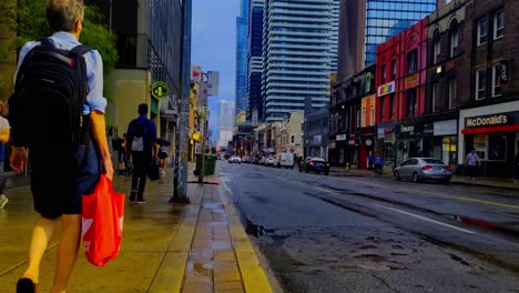 Escena-De-La-Calle-Después-De-La-Lluvia-Caída-Peatones-Gordos-Tráfico-Ciclista-Nivel-De-Los-Ojos-Calle-Wellesley-Yonge-Edificios-Antiguos-De-Ladrillo-En-Primer-Plano-Eclipsados-Por-La-Moderna-Arquitectura-De-Vidrio-En-El-Fondo