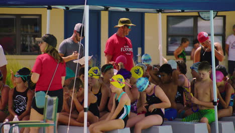 Children-on-swimsuit-and-caps-gather-by-swimming-pool-in-aquatic-center