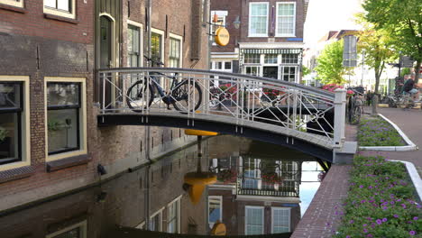 Bicicleta-Estacionada-En-El-Puente-Sobre-El-Canal-Con-Reflejos-En-El-Agua-En-Gouda,-Países-Bajos