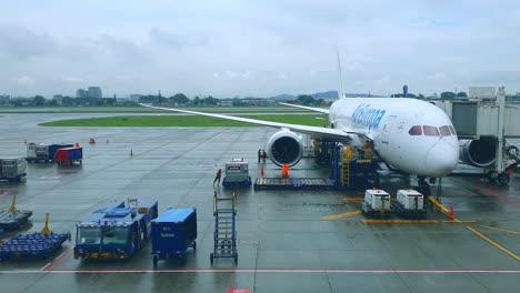 Avión-Transportado-Timelapse-Por-La-Tripulación-Que-Opera-El-Cargador-De-Contenedores-Antes-De-La-Salida-Y-El-Despegue-En-Un-Día-Lluvioso-Con-Equipos-Y-Tripulaciones-De-Apoyo-En-Tierra