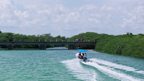 Drone-follows-speed-boat-racing-upstream-heading-below-concrete-brdgde-in-mangrove-forest-of-Tulum
