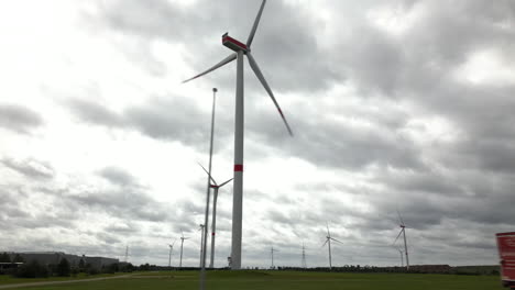 Wind-turbines-spinning-against-grey-moody-sky,-view-from-driving-car