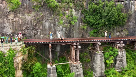 Panoramic-drone-footage-of-several-tourists-exploring-the-Thailand-Burma-Railway,-also-known-as-the-Death-Railway,-that-was-constructed-by-WWII-POWs-beginning-in-1942-in-Kanchanaburi,-Thailand