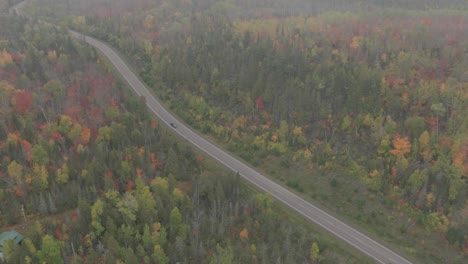 Luftaufnahme-Eines-Autos,-Das-Mitten-Im-Herbstwald-Die-Straße-Hinunterfährt,-Drohne,-Die-In-Nebligen-Nebel-Eindringt