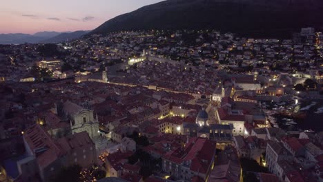 Croatia-Aerial:-Dubrovnik-at-dusk,-highlighting-terracotta-rooftops-and-mountain-backdrop