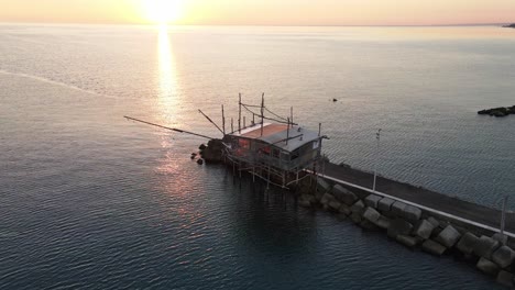 Aerial-landscape-view-over-a-trabucco,-traditional-fishing-machine,-on-the-italian-seashore,-at-sunset