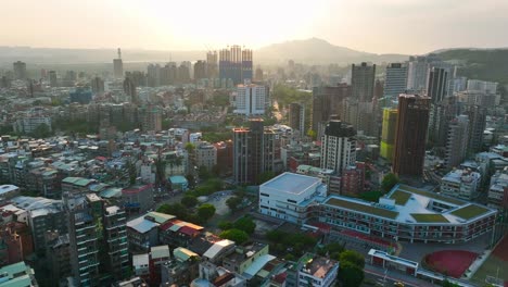 Aerial-flyover-wealthy-tienmu-district-in-Taipei-City-with-golden-sunset-in-background,-Taiwan---Drone-establishing-flight