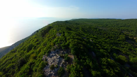 Drone-soars-along-exposed-rocky-cliff-edge-of-Lubenice-Croatia,-sunset-over-ocean