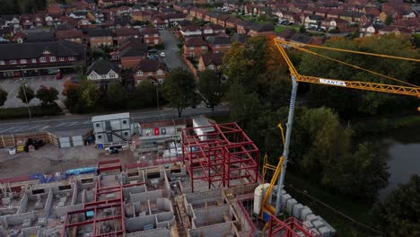 Aerial-view-rising-back-from-crane-on-care-home-construction-development-in-rural-British-village-next-to-fishing-lake