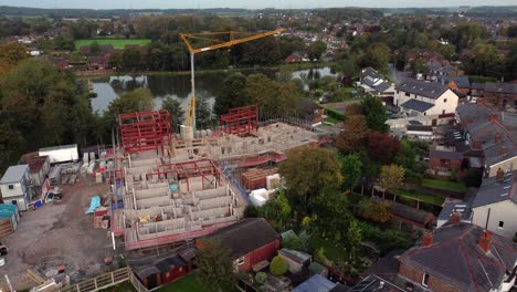 Aerial-view-towards-crane-building-waterside-care-home-construction-framework-in-rural-British-village-next-to-fishing-lake