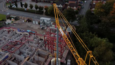 Aerial-view-Birdseye-above-crane-on-care-home-construction-development-site-in-rural-British-village-next-to-fishing-lake