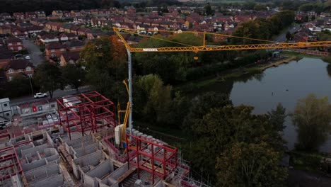 Aerial-view-rising-over-crane-on-waterside-care-home-development-in-rural-British-village-next-to-fishing-lake