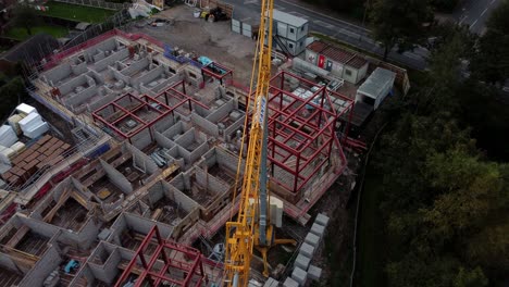 Aerial-flyover-view-of-crane-on-care-home-construction-development-site-in-rural-British-village-next-to-fishing-lake
