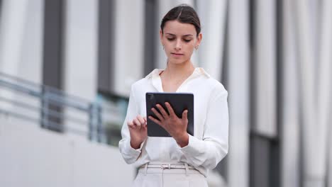businesswoman-walking-past-a-modern-building-while-working-on-her-tablet