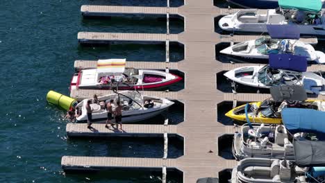 several-people-relaxing-on-a-boat-while-its-still-docked-on-lake-arrowhead-california-crystal-clear-blue-water-sunny-day-kids-having-fun-yacht-boat-pontoon-AERIAL-STATIC