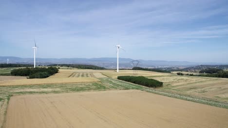 Slow-moving-drone-shot-of-farming-landscape-and-windmills-with-mountains-and-a-city-in-the-background