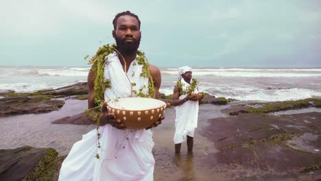 Cerca-De-2-Tradicionalistas-Africanos-Ga-Sosteniendo-Calabaza-Realizando-Rituales-Y-Libaciones-En-Las-Rocas-Al-Lado-Del-Mar.