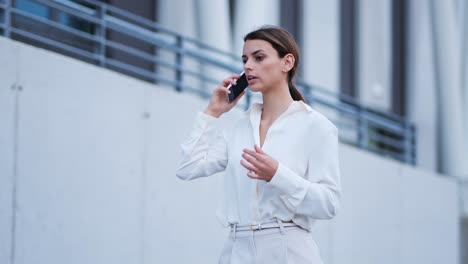 A-businesswoman-walks-along-a-wall-while-talking-on-her-cell-phone