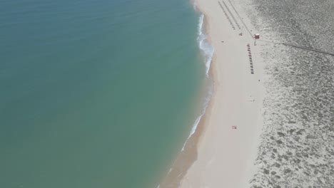 Luftaufnahme-Eines-Sandigen,-Gelben-Strandes-Mit-Sonnenschirmen-Am-Ufer