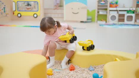 Little-girl-playing-in-children's-playroom---loading-toy-excavator-bucket-with-wooden-small-cubes,-tectile