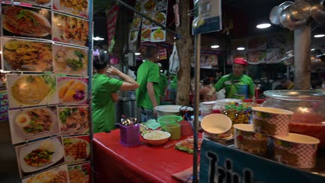 Beim-Kochen-Und-Verkaufen-Von-Speisen-Auf-Dem-Chatuchak-Wochenendnachtmarkt-Bieten-Straßenhändler-Eine-Große-Auswahl-An,-Darunter-Scharf-Gebratener-Tintenfisch,-Hühnchen,-Hotdogs-Und-Vieles-Mehr.-Sie-Befinden-Sich-In-Bangkok,-Thailand