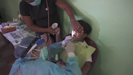 Dentist-woman-applies-anesthesia-to-perform-a-procedure-on-a-child's-teeth-during-a-medical-brigade-in-an-improvised-clinic,-in-a-poor-community-school