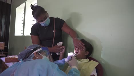 Female-dentist-applies-anesthesia-to-perform-a-procedure-on-a-child's-teeth-during-mobile-medical-brigade