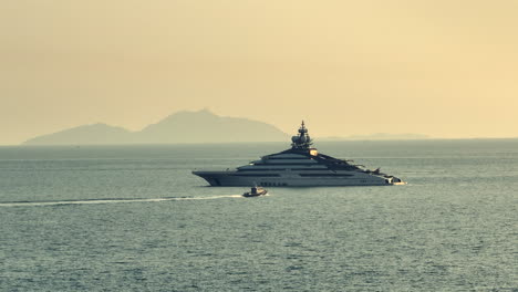 Private-super-yacht-anchored-at-sea-of-Hong-Kong-City---Coast-guard-boat-approaching---Aerial-view-during-foggy-sunset-time