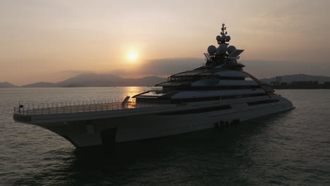 Drone-shot-showing-luxury-Nord-yacht-anchored-in-Hong-Kong-at-sea-during-golden-sunset---mountain-range-landscape-during-cloudy-day-in-the-evening