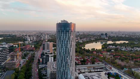 Rotating-Aerial-View-Of-A-Tall-Office-Building-With-A-Sunset-In-The-Background,-Bucharest,-Romania