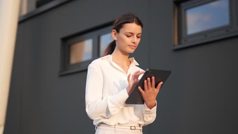 Businesswoman-walking-walking-past-modern-building-with-a-tablet-in-her-hand