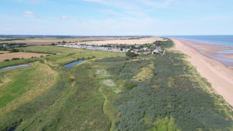 High-above,-video-footage-offers-a-scenic-view-of-the-saltwater-marshes-along-the-Lincolnshire-coast,-with-seabirds-soaring-and-resting-on-the-lagoons-and-inland-lakes