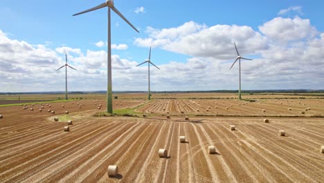 High-above,-the-camera-records-the-tranquil-scene-of-wind-turbines-spinning-gracefully-in-a-Lincolnshire-farmer's-field,-recently-harvested-and-adorned-with-golden-hay-bales