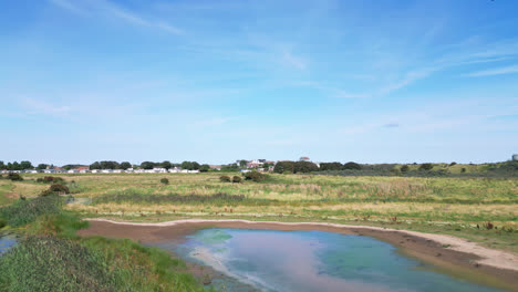 Above-the-coastal-terrain,-video-footage-offers-a-view-of-the-tranquil-saltwater-marshes-of-the-Lincolnshire-coast,-with-seabirds-gracefully-flying-and-resting-on-the-lagoons-and-inland-lakes