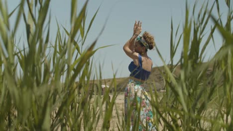 Rack-focus-from-between-reeds-of-happy-European-woman-dancing-hands-in-air