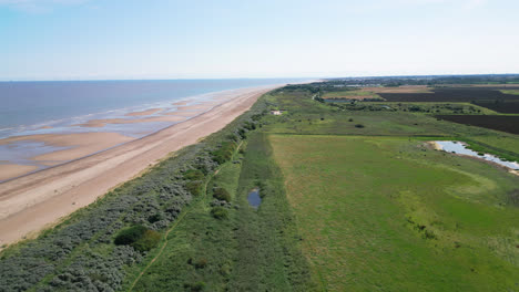 Video-from-above-captures-the-splendor-of-the-saltwater-marshes-along-the-Lincolnshire-coast,-showcasing-seabirds-soaring-and-perching-on-the-lagoons-and-inland-lakes