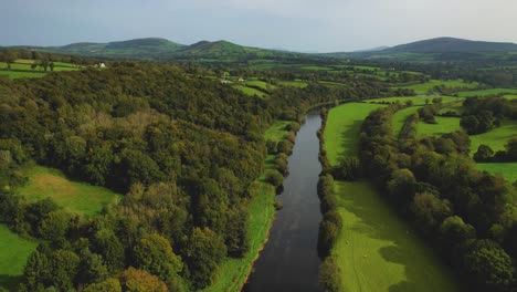 Eine-4K-Drohne-Zeigt-Eine-Aufnahme-Des-Flusses-Nore,-Der-Langsam-In-Richtung-Des-Dorfes-Inistioge-County-Kilkenny,-Irland,-Fließt,-Wobei-Die-Brücke,-Die-Zum-Dorf-Führt,-Nicht-Weit-Entfernt-Schafe-Grasen-In-Der-Nähe