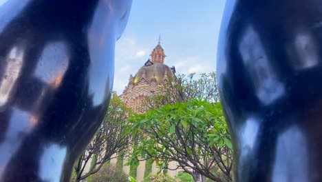 Fernando-Botero-square-main-building-through-legs-of-his-sculpture-in-Medellin,-Colombia