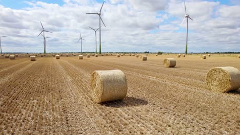 Luftaufnahmen-Bieten-Einen-Atemberaubenden-Anblick:-Eine-Reihe-Von-Windturbinen,-Die-Sich-Auf-Dem-Frisch-Abgeernteten-Feld-Eines-Bauern-Aus-Lincolnshire-Drehen,-Mit-Goldenen-Heuballen-Im-Vordergrund