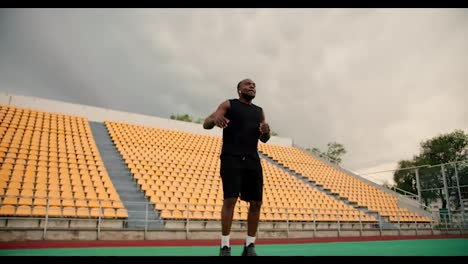 Un-Atleta-De-Piel-Negra-Con-Uniforme-Deportivo-Negro-Está-Calentando-En-El-Estadio-Levantando-Las-Piernas-Lo-Más-Alto-Posible-Mientras