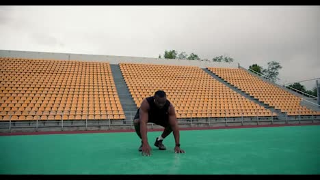 Un-Hombre-Negro-Con-Ropa-Deportiva-Negra-Haciendo-Un-Ejercicio-De-Burpee-En-Un-Estadio-Con-Gradas-Amarillas