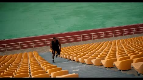 Un-Atleta-De-Piel-Negra-Con-Un-Uniforme-Deportivo-Negro-De-Verano-Corre-En-Las-Gradas-De-Arriba-Del-Estadio-Con-Sillas-Amarillas