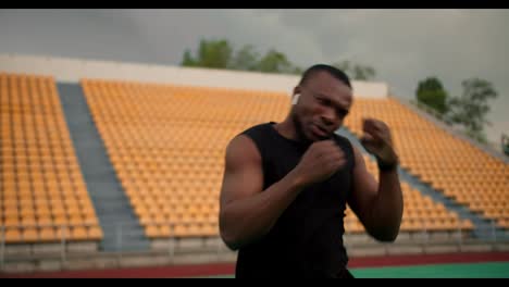 Close-up-shot-of-an-athlete-with-Black-skin-color-in-a-black-sports-uniform-boxing-in-a-stadium-with-yellow-chairs-in-the-stands