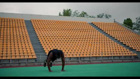 Entrenamiento-En-El-Campo-Deportivo.-Un-Hombre-Negro-Con-Ropa-Deportiva-Negra-Haciendo-Un-Ejercicio-De-Burpee-En-Un-Estadio-Amarillo