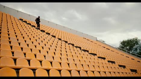 Un-Atleta-De-Piel-Negra-Con-Ropa-Deportiva-Negra-De-Verano-Baja-Las-Escaleras-Del-Estadio-Con-Sillas-Amarillas-En-El