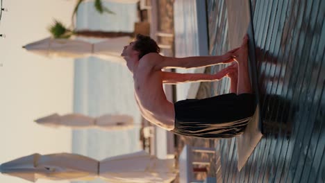 Young-naked-torso-yogi-in-black-shorts-doing-yoga-and-meditation-on-the-beach.-Morning-exercise-and-zen-style