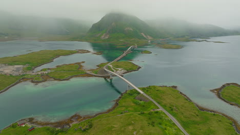 Aerial-panoramic-overview-of-Fredvang-Bridge,-low-hanging-misty-clouds-cover-mountain-ridgeline