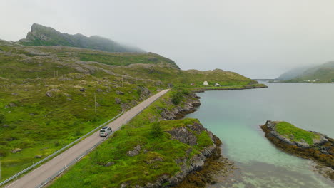 Adventure-camper-van-drives-along-scenic-Lofoten-Norway-highway-off-into-cloudy-mountains-in-distance