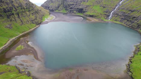 Drone-flying-over-Saksun's-lagoon-surrounded-by-mountains-in-Faroe-Islands